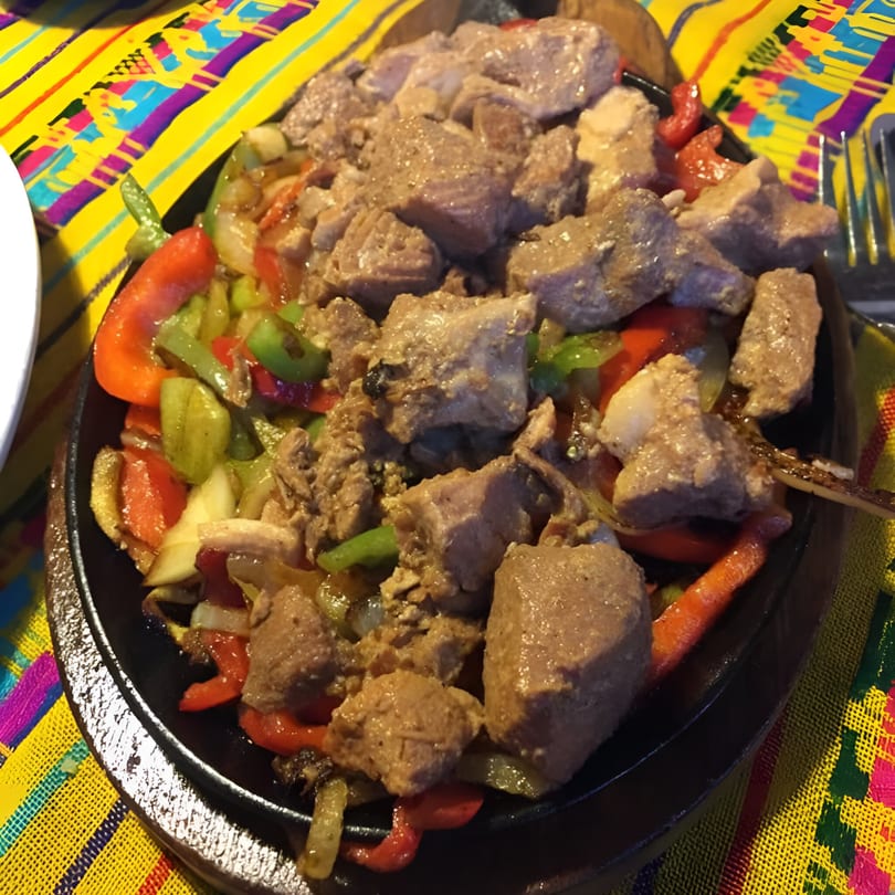 Sizzling Mexican fajitas with pork, red and green bell peppers, and onions on a black skillet.