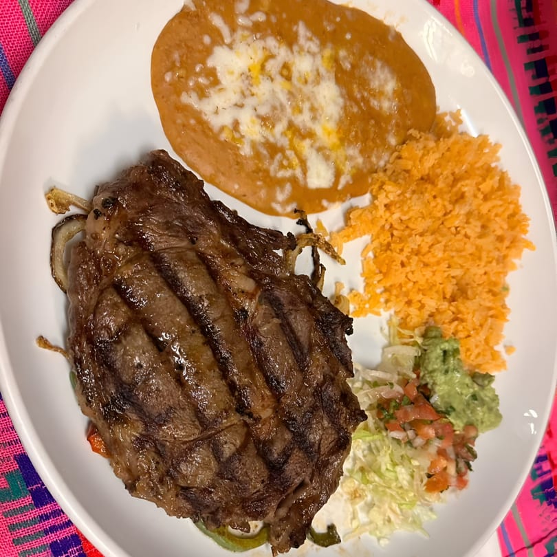 Grilled steak with refried beans, Mexican rice, guacamole, pico de gallo, and shredded lettuce.