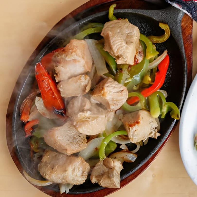 Sizzling chicken fajitas with red and green bell peppers and onions on a cast iron skillet.