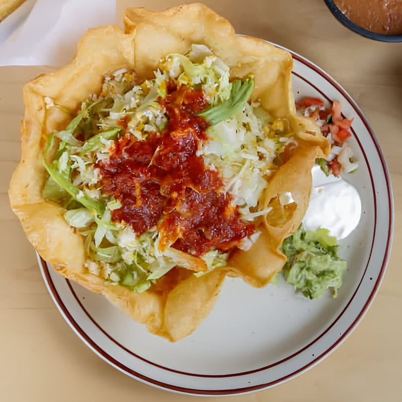 A Si Amigos taco salad in a crispy fried tortilla bowl with salsa, guacamole, and sour cream.